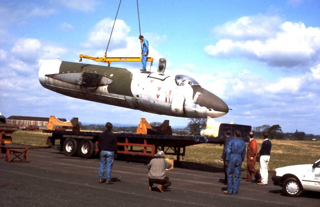 A crane lifts the Canberra fuselage off a trailer, while volunteers look on.