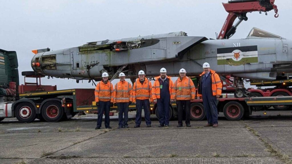 Volunteers stand in front of the Tornado ZA475 fuselage, which is sitting on a trailer.